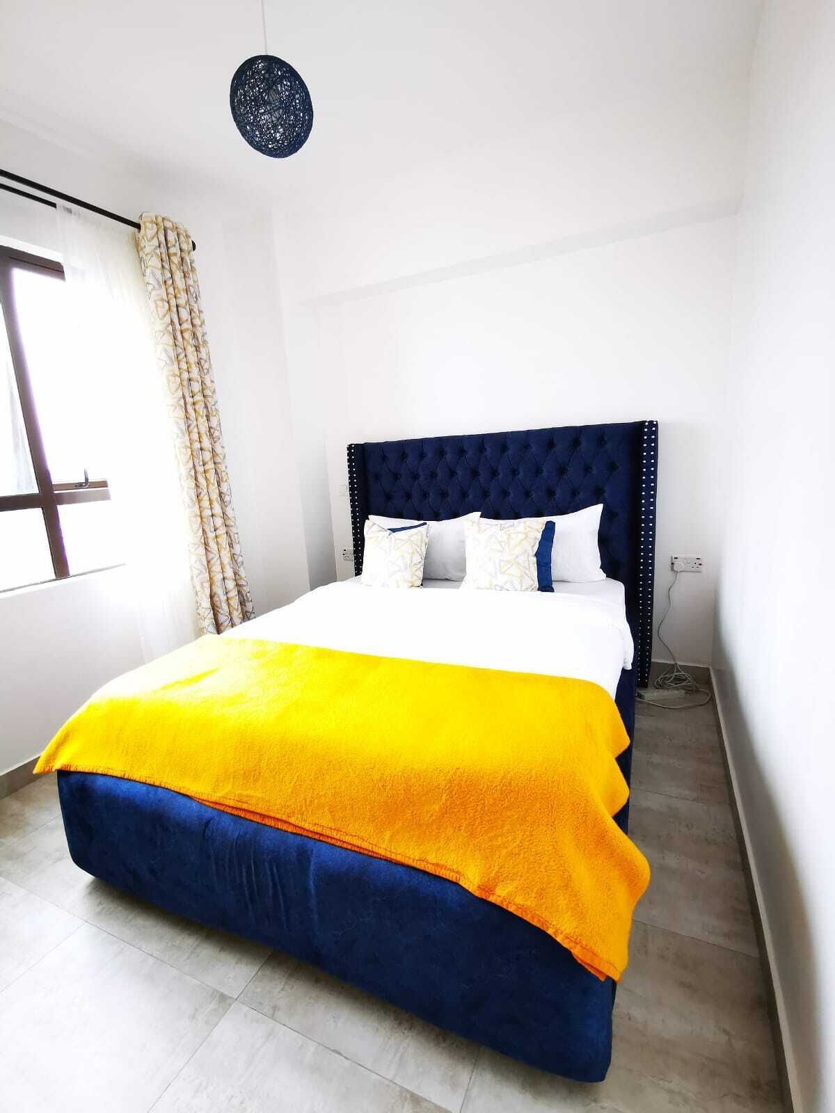 A bed with a blue headboard, white and blue pillows, and a yellow and blue blanket.