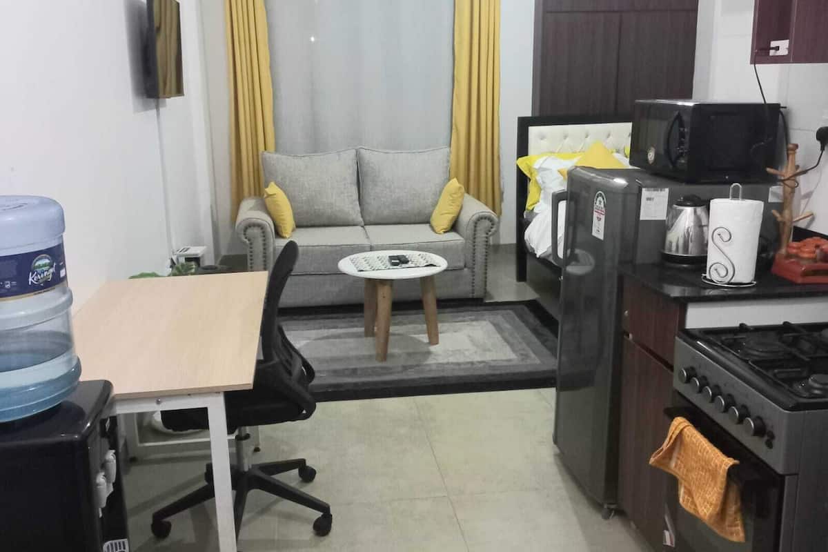 A compact living space with a kitchenette, a sofa, a small dining table, and a water dispenser.