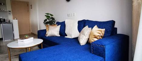 Una sala moderna con un sofá seccional azul, una mesa de centro blanca y una planta en maceta.