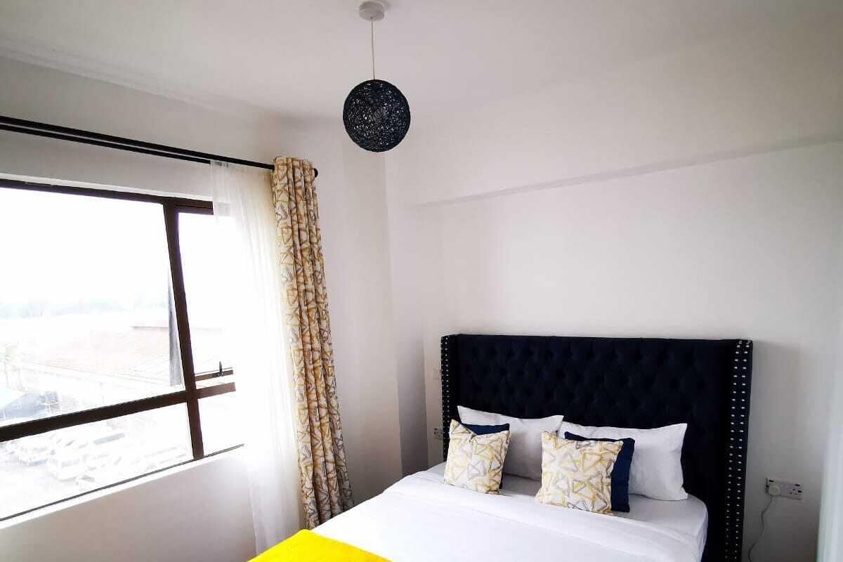 A hotel room with a large bed, a window with curtains, and a hanging light fixture.