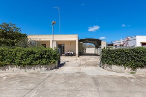 A building entrance with a covered walkway, a small outdoor seating area, and a clear blue sky. - 3847 Villetta Le Largure B by Barbarhouse (Melendugno)
