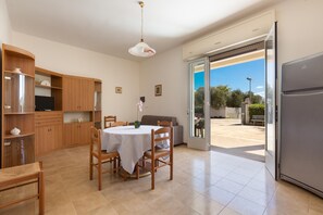 A spacious kitchen with wooden cabinets, a dining table, chairs, and a large sliding glass door leading to an outdoor area. - 3847 Villetta Le Largure B by Barbarhouse (Melendugno)