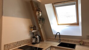 A kitchen with a built-in stove, a sink, a window, and a shelf with kitchen items. - En Campagne un Petit Studio Douillet, Tout Équipé, à Deux pas D'azay le Rideau (Cheillé)