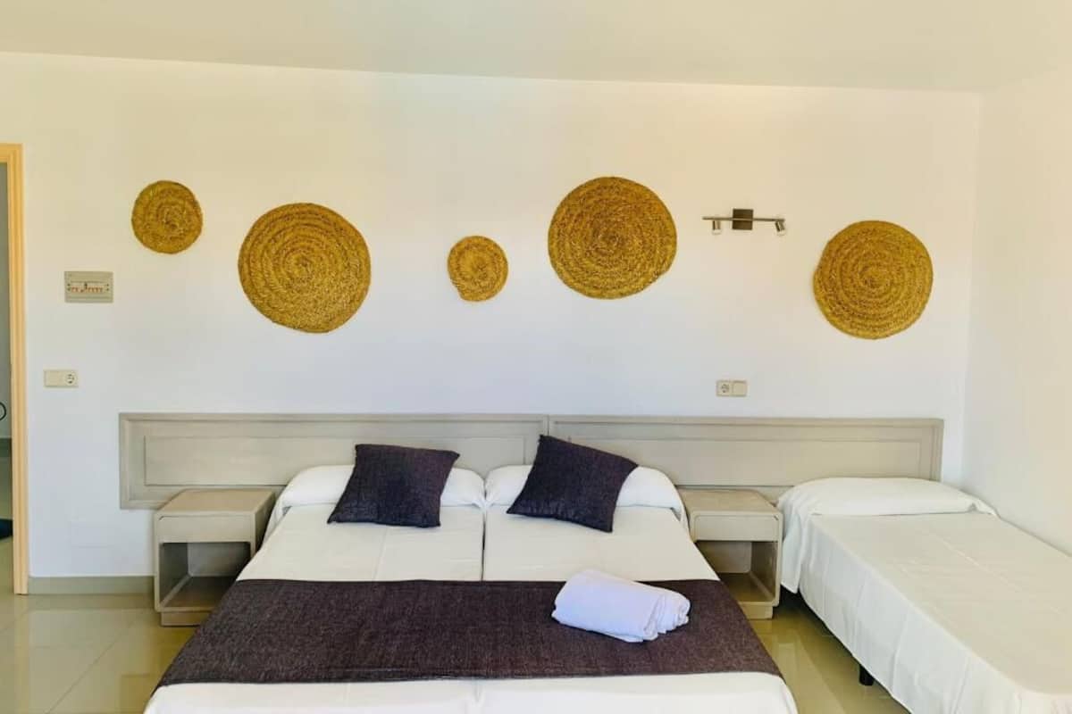 A hotel room with two beds, a large bed with a dark throw blanket and pillows, and a smaller bed with a white bedspread.