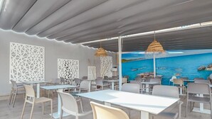 An outdoor dining area with tables and chairs, a view of the sea, and decorative white panels. - Hotel Lliteras (Capdepera)