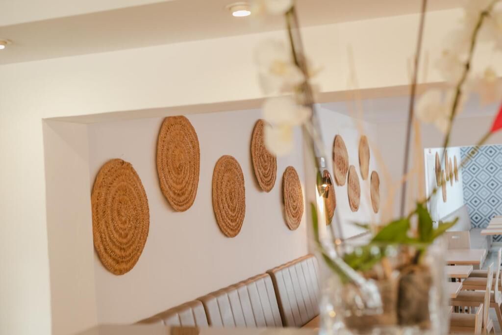 A dining area with a long table, white chairs, and a wall decorated with circular woven art pieces.