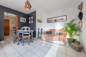 En moderne stue med spiseplads, der indeholder en sofa, et spisebord med stole, en potteplante og dekorationer på væggen.