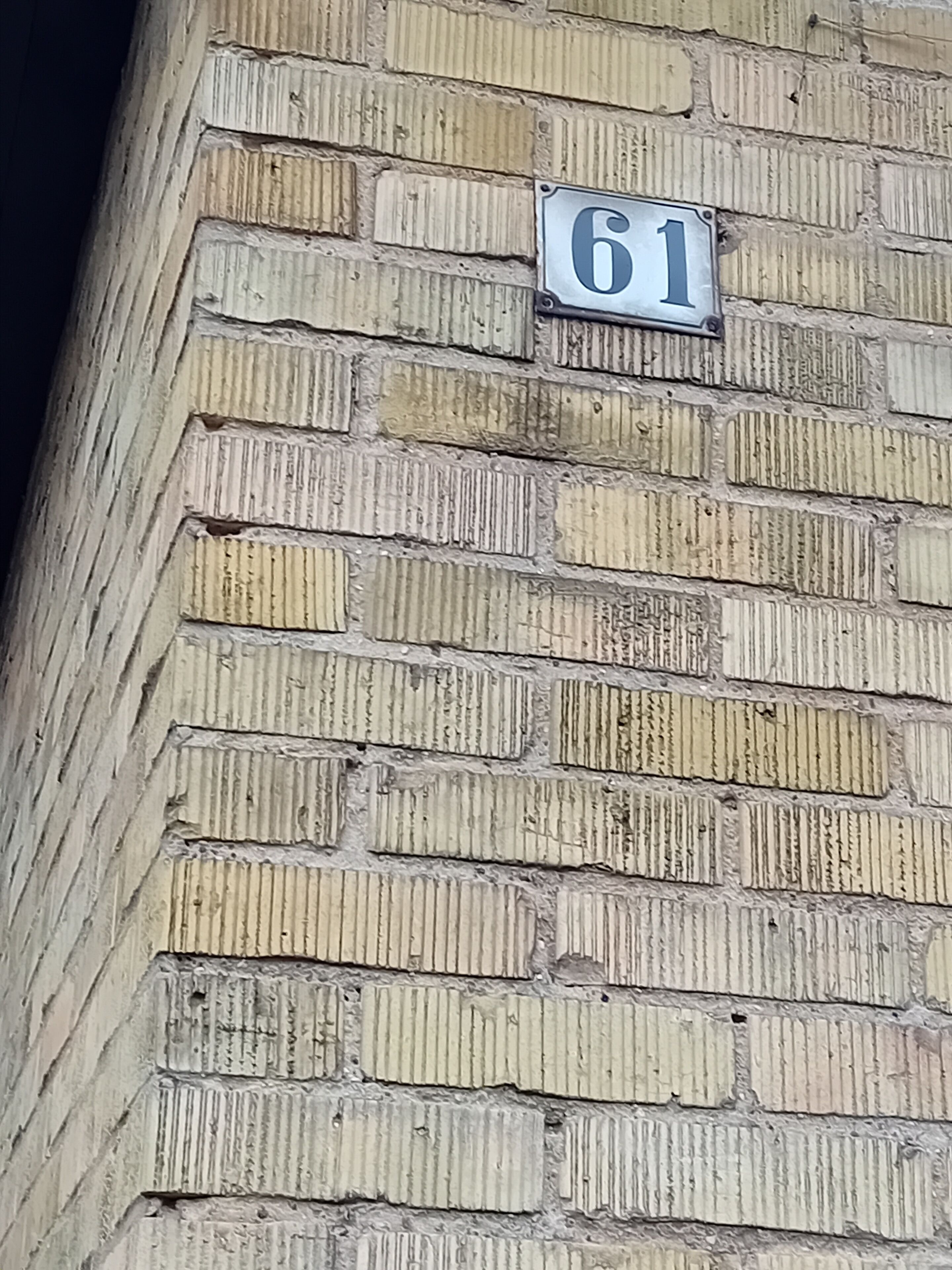 A brick wall with a house number sign displaying '61'.
