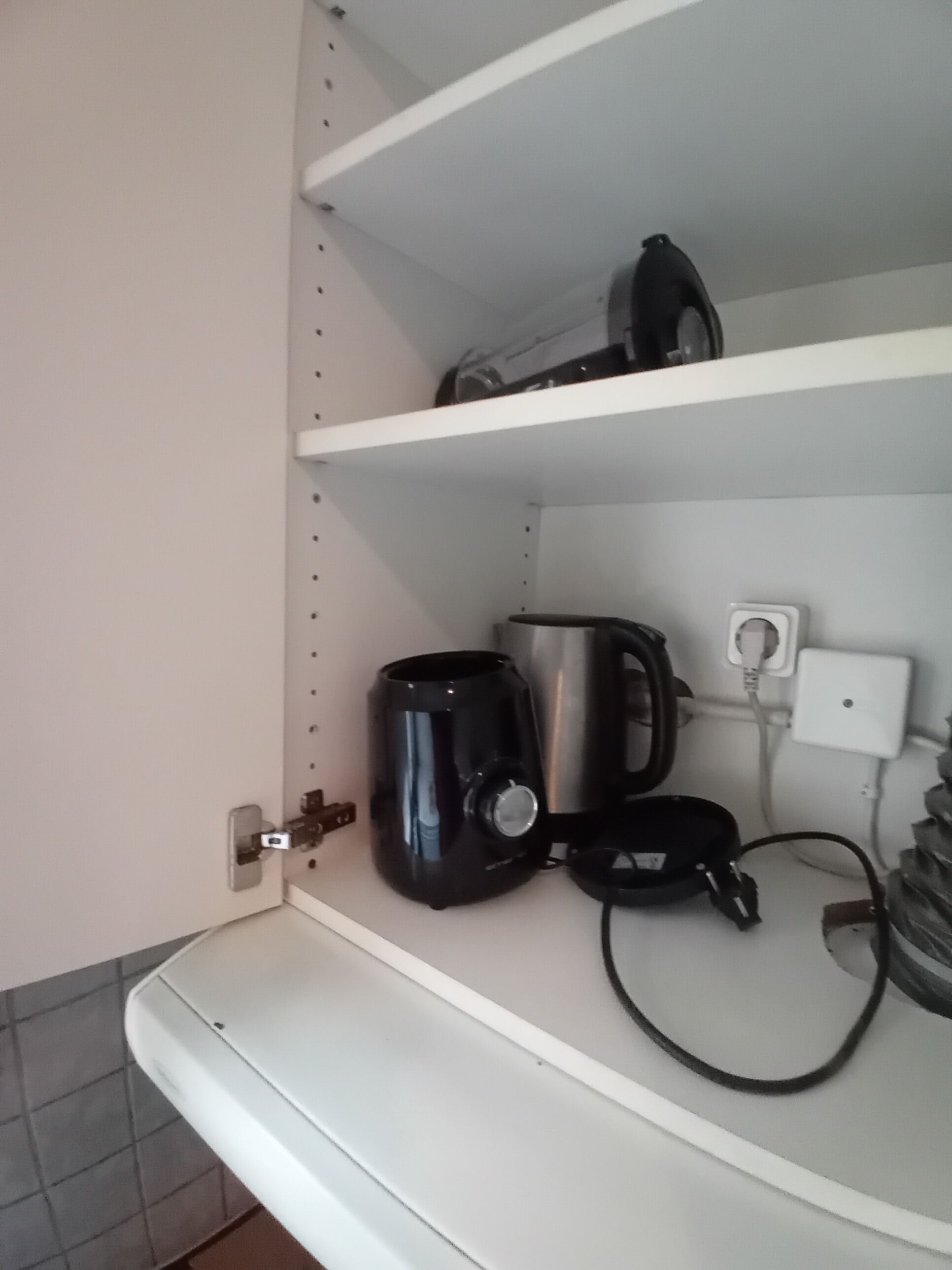 Una cocina con estantes blancos, una cafetera, un hervidor y un enchufe.