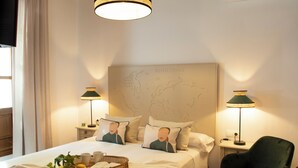 A neatly made bed with a map headboard, two bedside lamps, and a green chair.