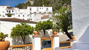 A terrace with white tables and chairs, potted plants, and a view of a mountain with a castle.