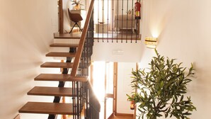 A wooden staircase with a railing, a potted plant, and a light fixture on the wall.