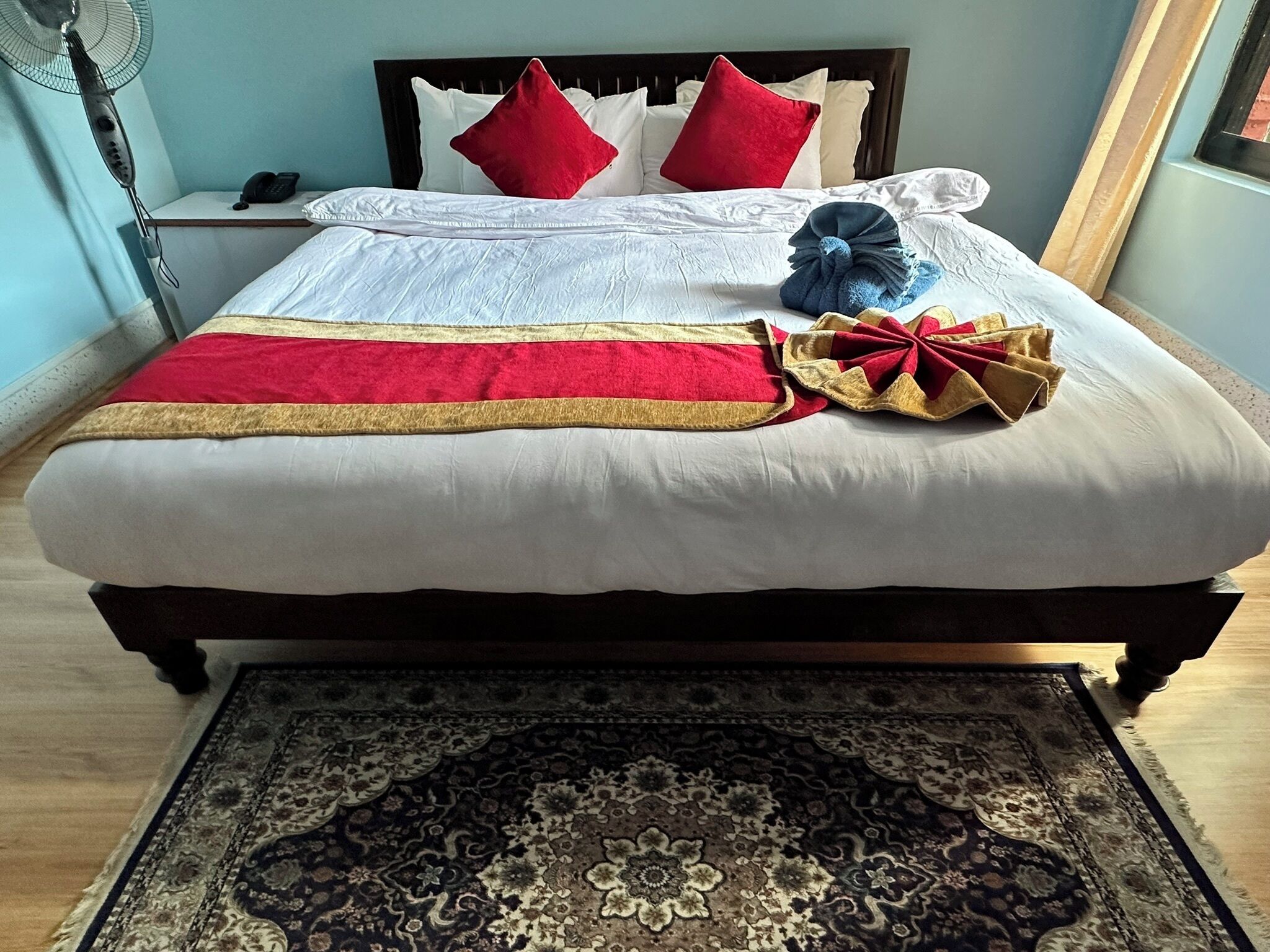 A neatly made bed with a red and gold bedspread, a blue towel, and red pillows.