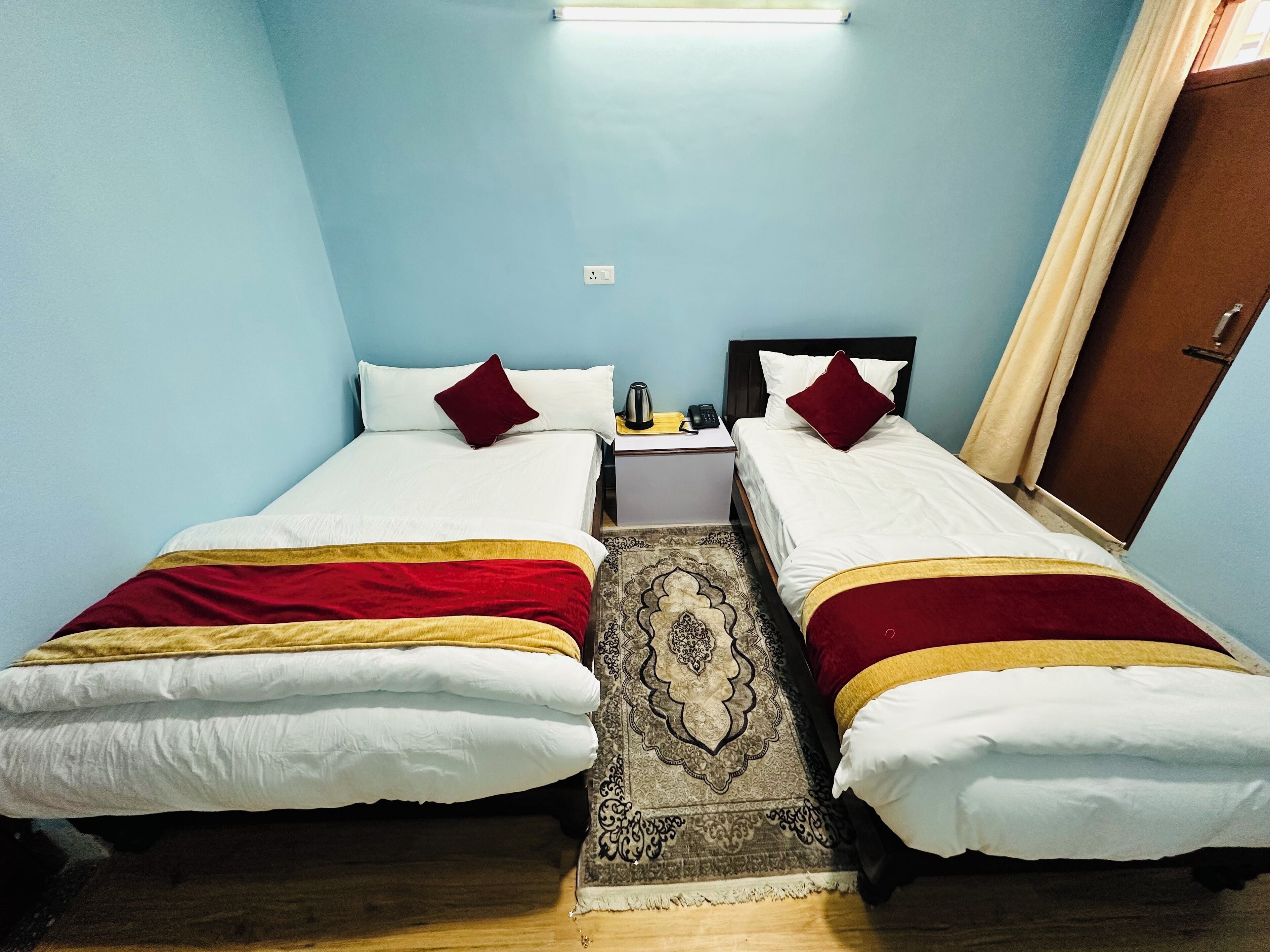 Ein Doppelzimmer mit zwei Betten, einem Nachttisch, einem gemusterten Teppich und einer Tür.
