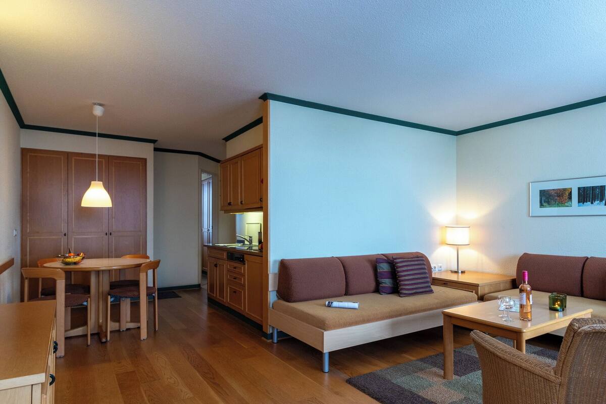 A compact living space with a dining area, kitchenette, sofa, and a small table with a lamp.