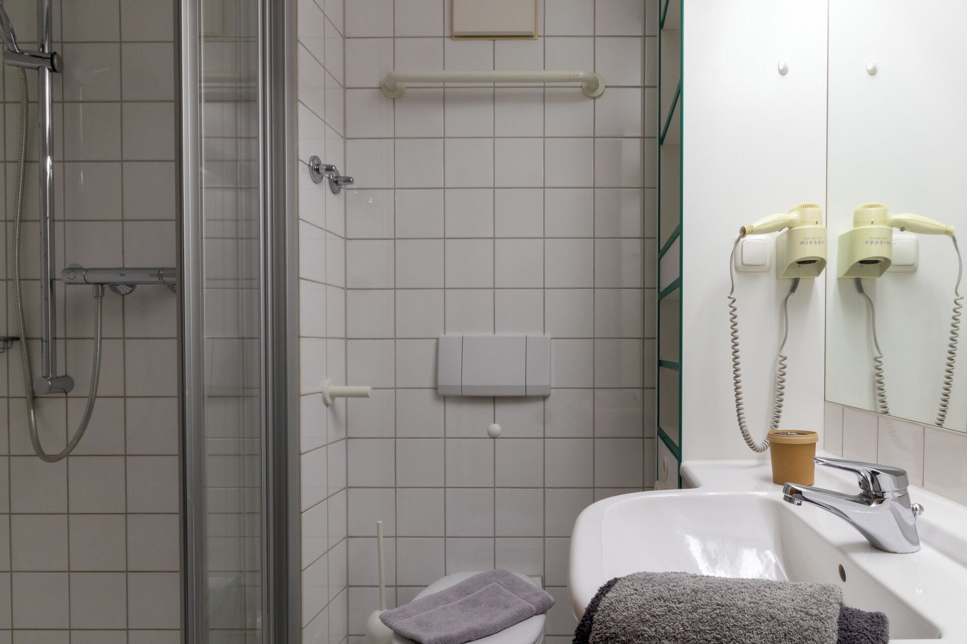 Une salle de bain avec une douche à parois de verre, un lavabo blanc et un miroir équipé d’un sèche-cheveux.
