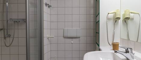 Une salle de bain avec une douche à parois de verre, un lavabo blanc et un miroir équipé d’un sèche-cheveux.