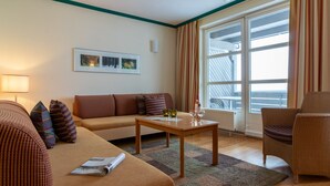 A living room with a sofa, armchair, and a table with glasses and a bottle. - UplandParcs Bergresidence (Winterberg)