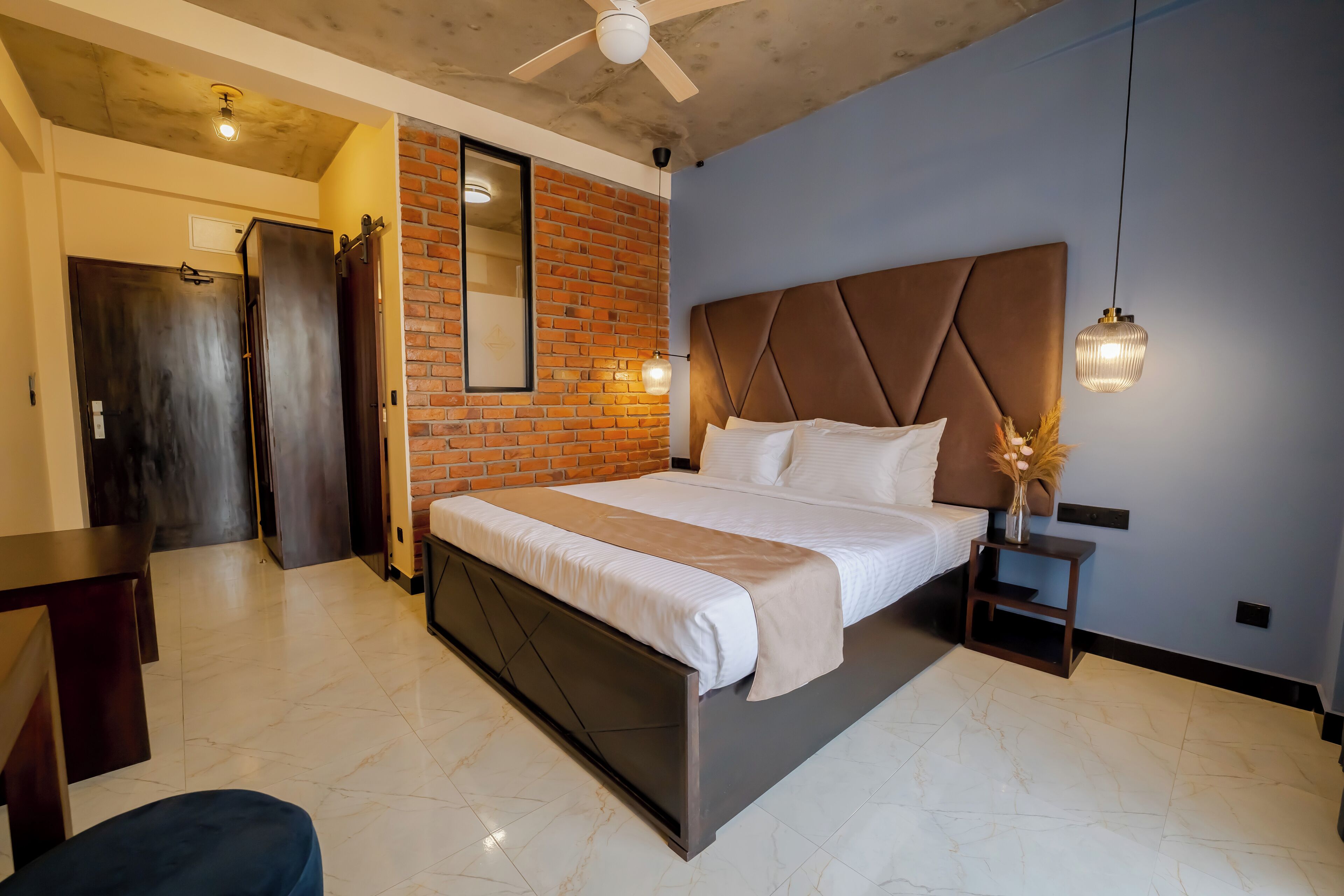 A modern bedroom with a large bed, a brick accent wall, and a ceiling fan.