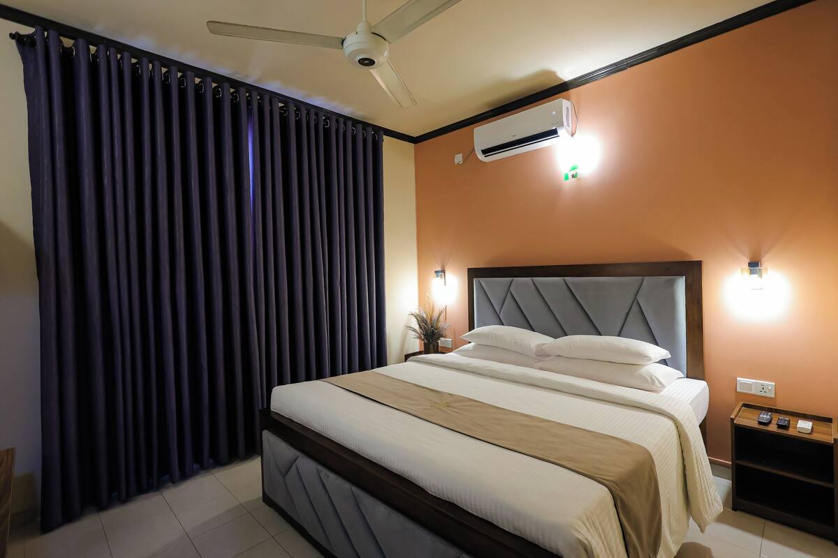 Ein Hotelzimmer mit Bett, Deckenventilator, Klimaanlage, Nachttisch und Wandlampe.