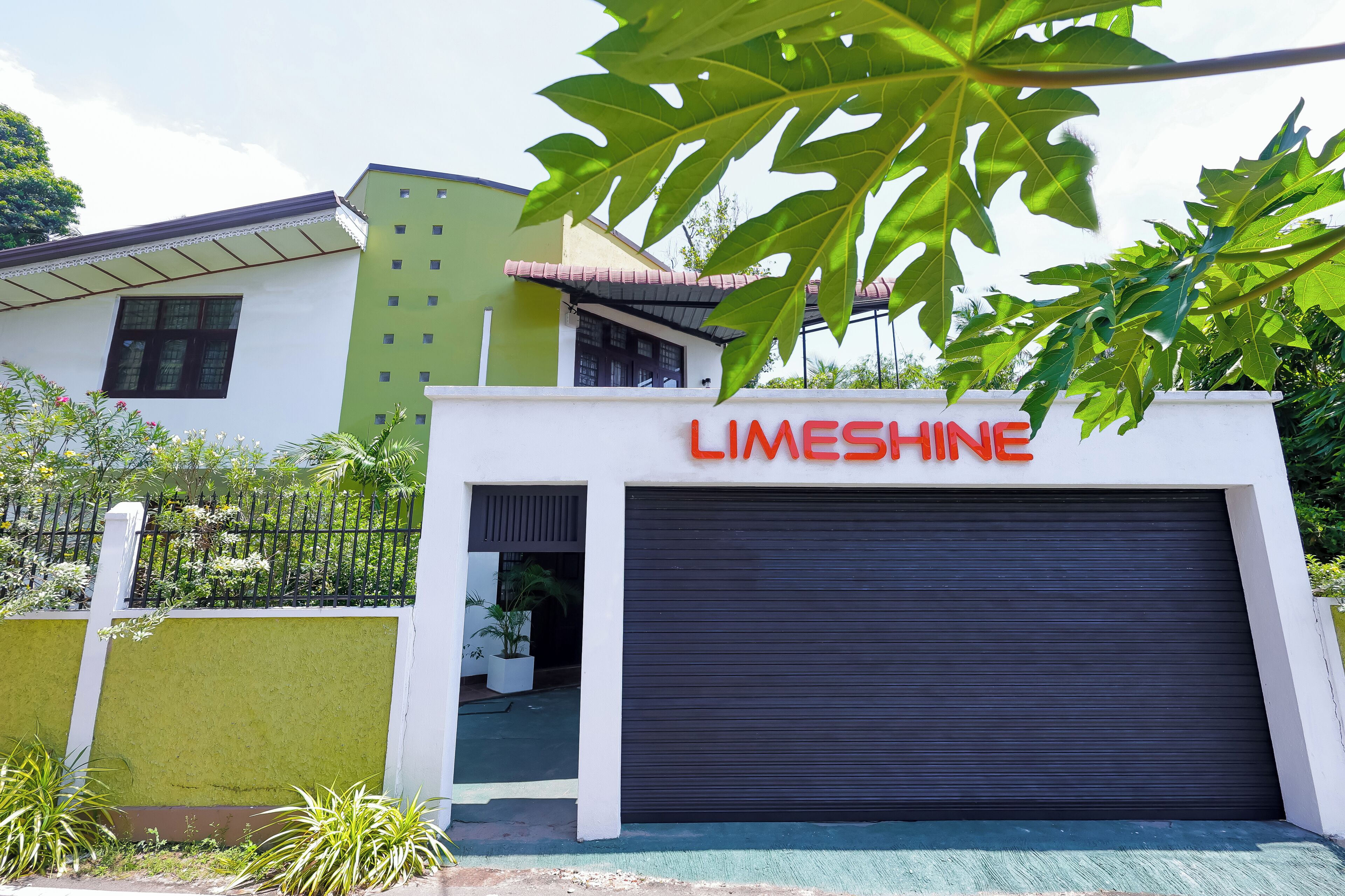 Un edificio con fachada verde y blanca, una puerta de garaje cerrada y un letrero que dice "LIMESHINE".