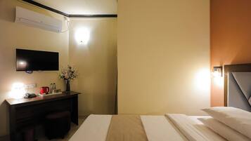 A hotel room with a bed, a desk with a lamp, a TV, and a wall-mounted air conditioner.