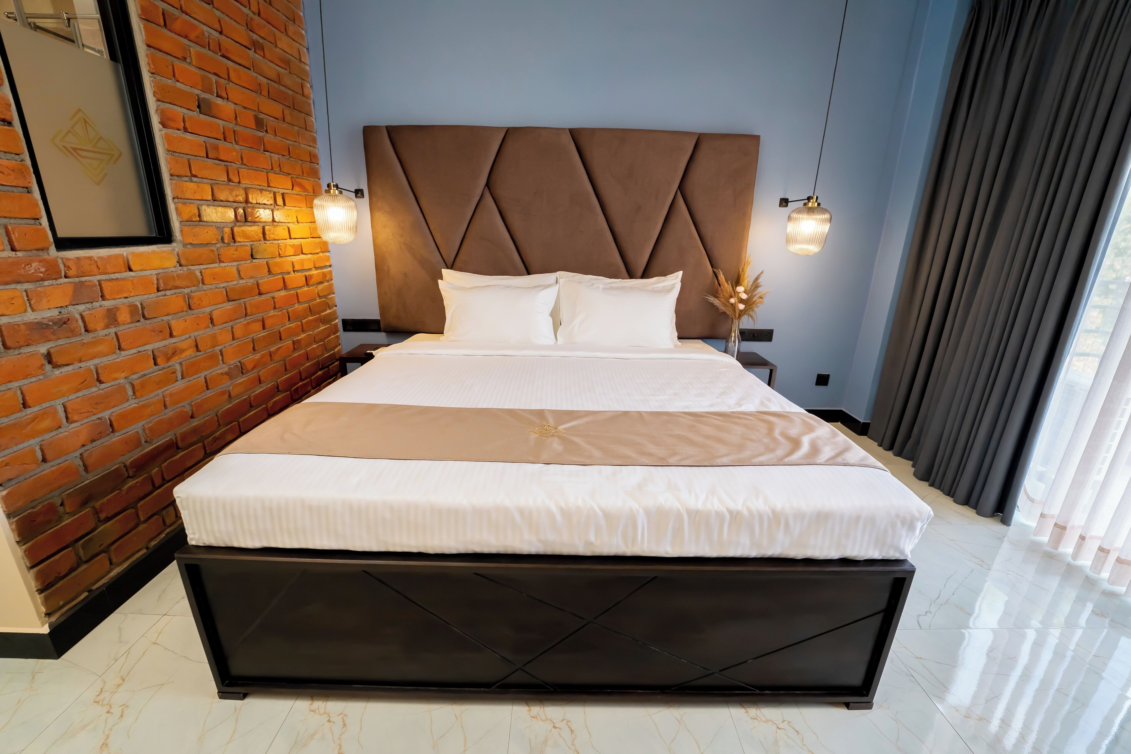 A modern hotel room with a brick wall, a large bed with a headboard, and two pendant lights.
