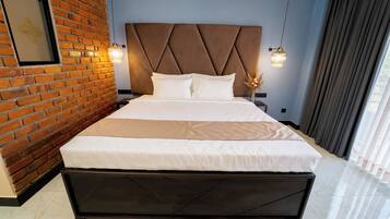 Quarto de hotel moderno com parede de tijolos, uma cama grande com cabeceira e duas luminárias pendentes.