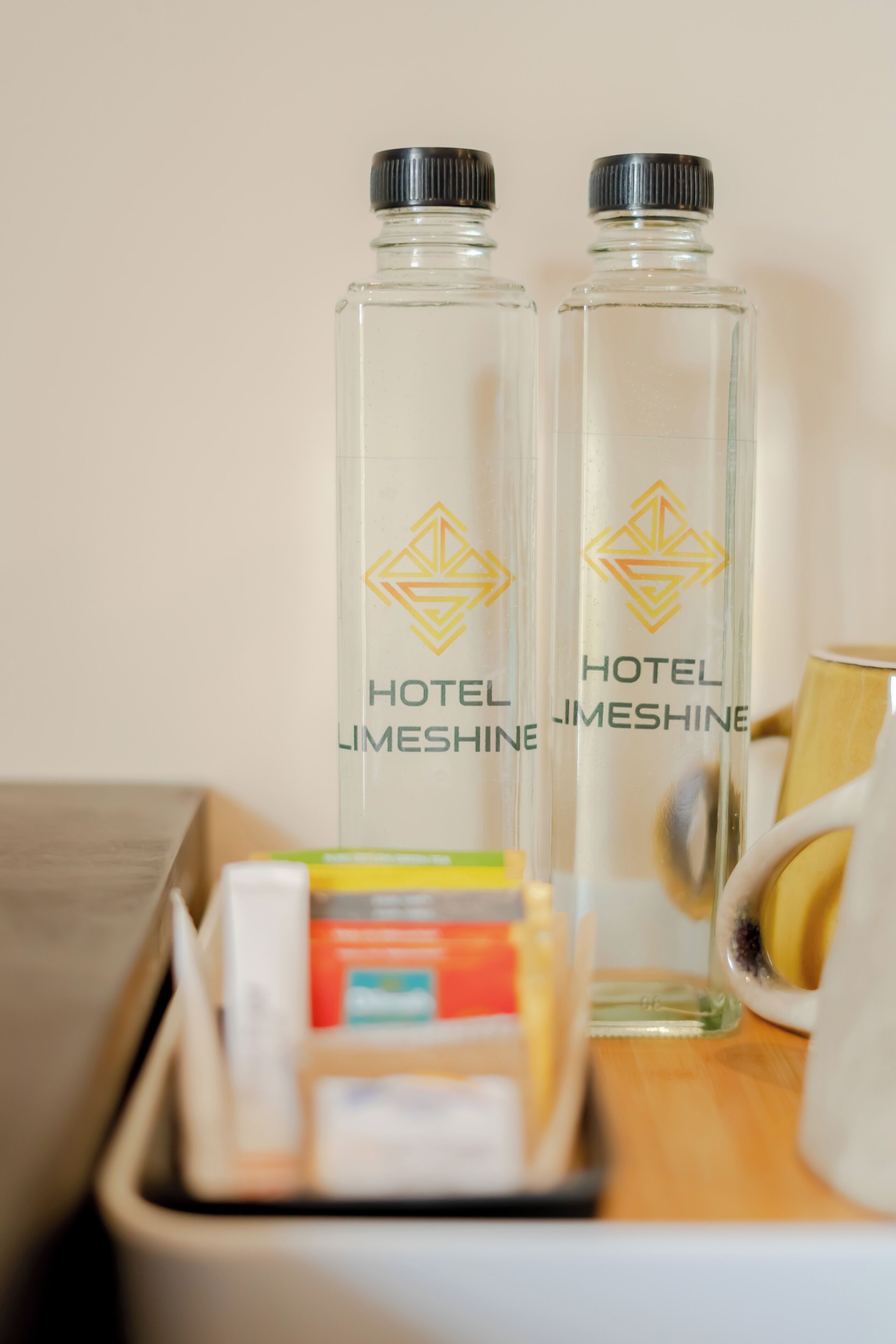 Two clear glass bottles with black caps and a hotel logo, placed on a wooden surface with a white tray containing various items.