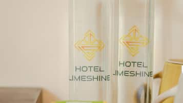 Deux bouteilles en verre transparent, dotées de bouchons noirs et ornées du logo d’un hôtel, sont posées sur une surface en bois, accompagnées d’un plateau blanc contenant divers objets.