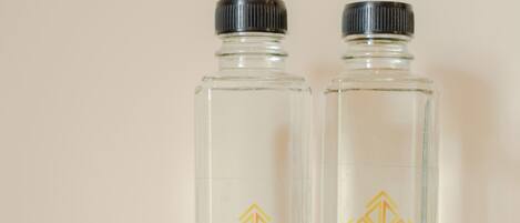Two clear glass bottles with black caps and a hotel logo, placed on a wooden surface with a white tray containing various items.