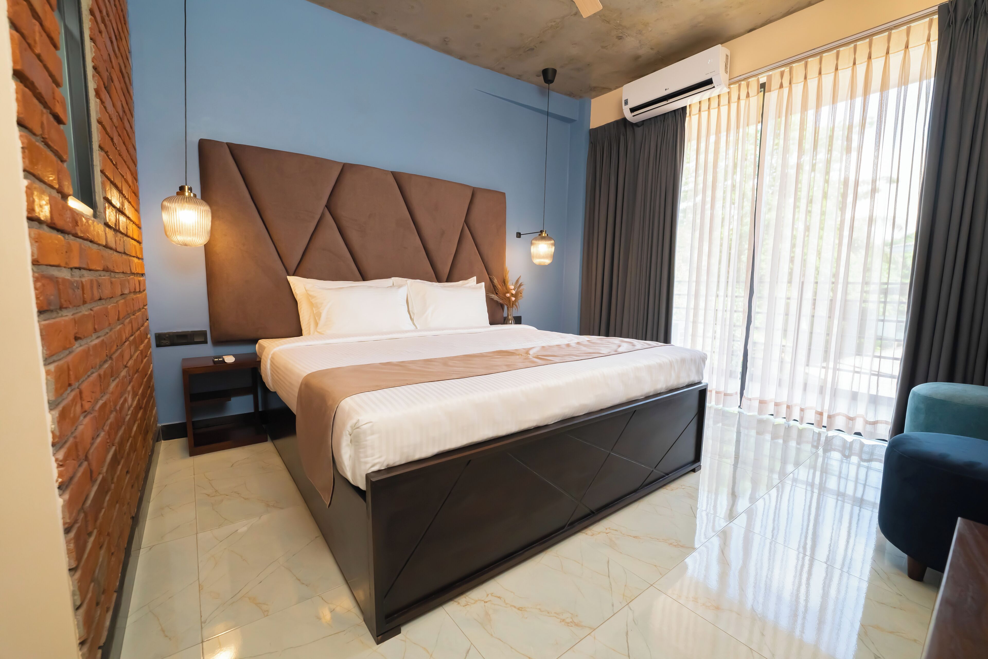 Une chambre d’hôtel moderne avec un grand lit, un mur en briques et une grande fenêtre avec des rideaux.