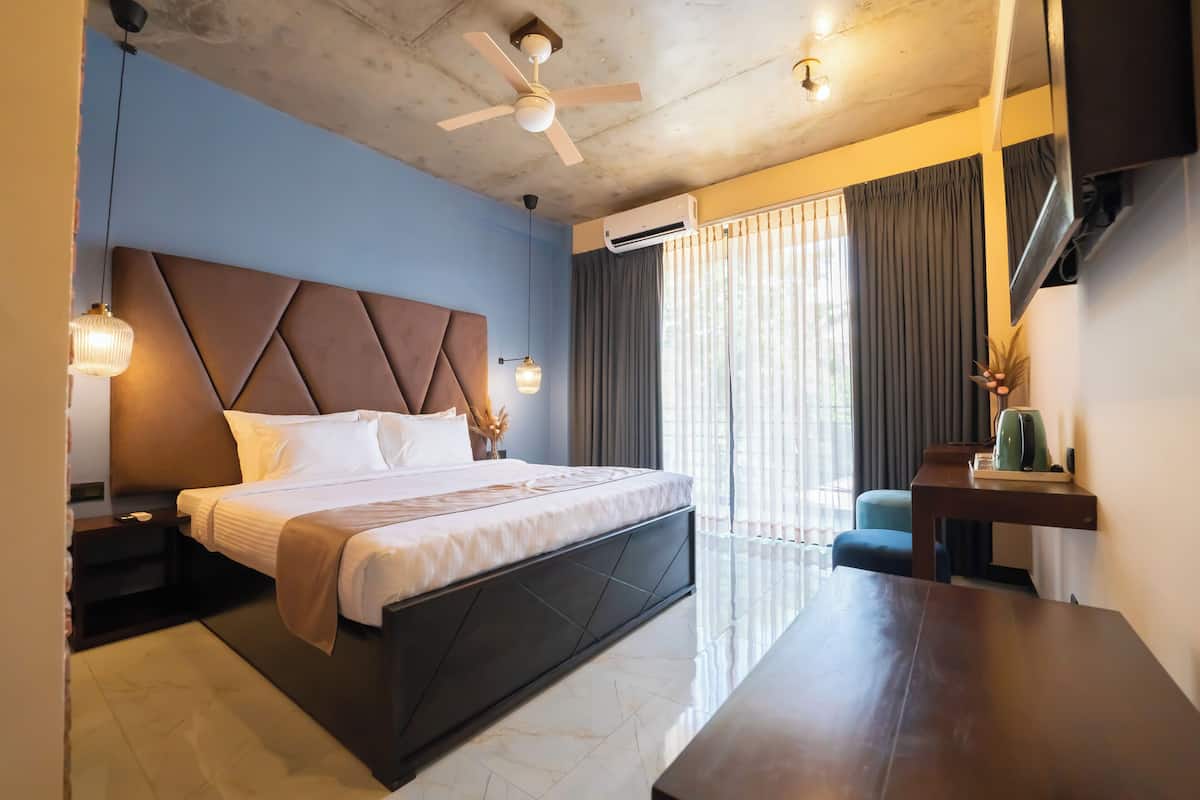 Ein modernes Hotelzimmer mit einem großen Bett, einem Schreibtisch, einem Deckenventilator und Blick ins Freie durch große Fenster.