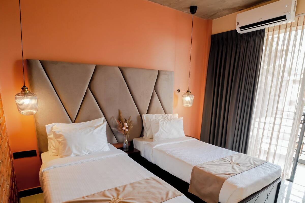 Ein Hotelzimmer mit zwei Betten, einem Deckenventilator, einer Klimaanlage und einem großen Fenster mit Vorhängen.