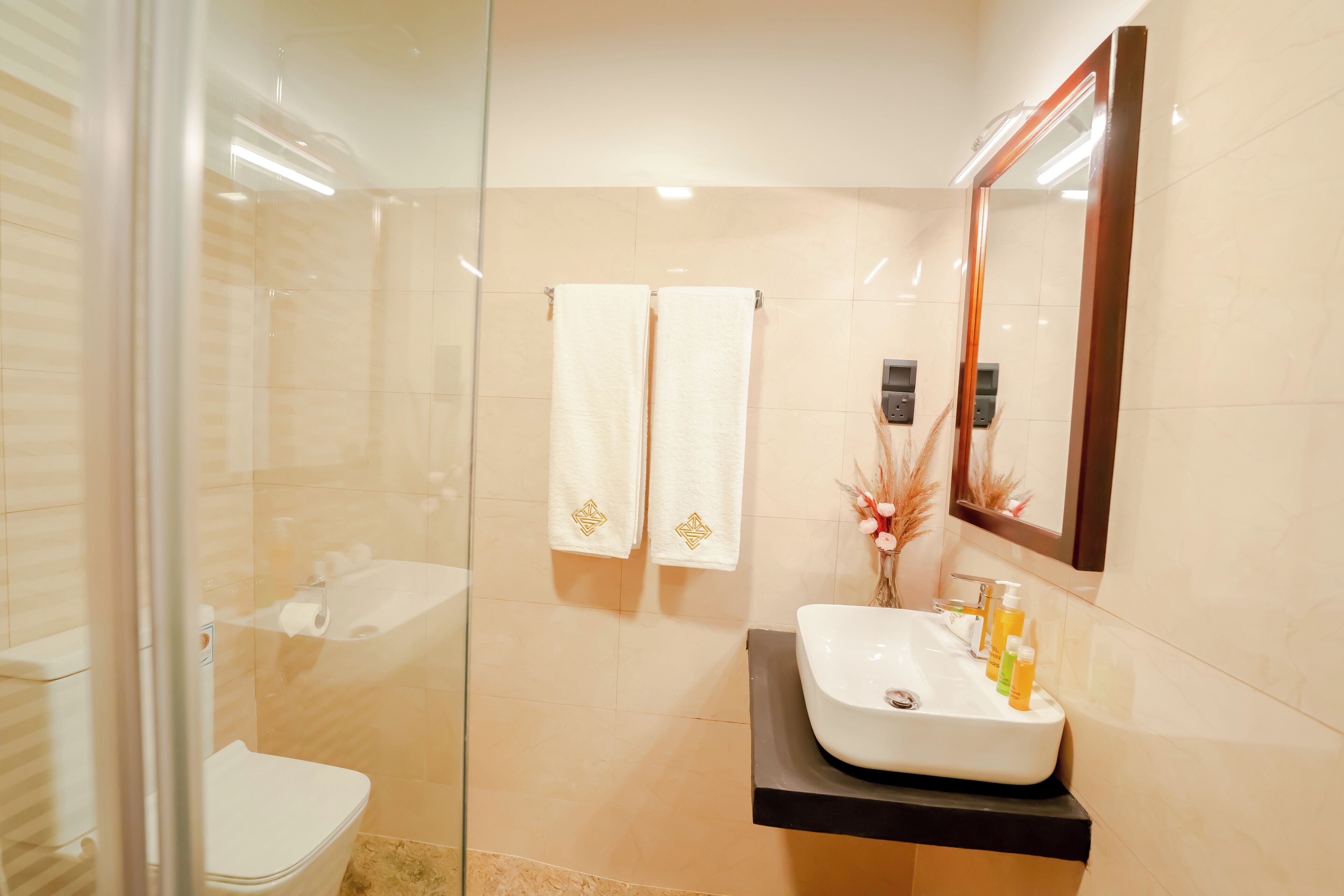 A modern bathroom with a glass shower enclosure, a white sink with toiletries, and a mirror above the sink.