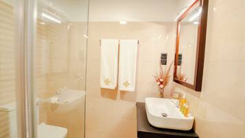 A modern bathroom with a glass shower enclosure, a white sink with toiletries, and a mirror above the sink.
