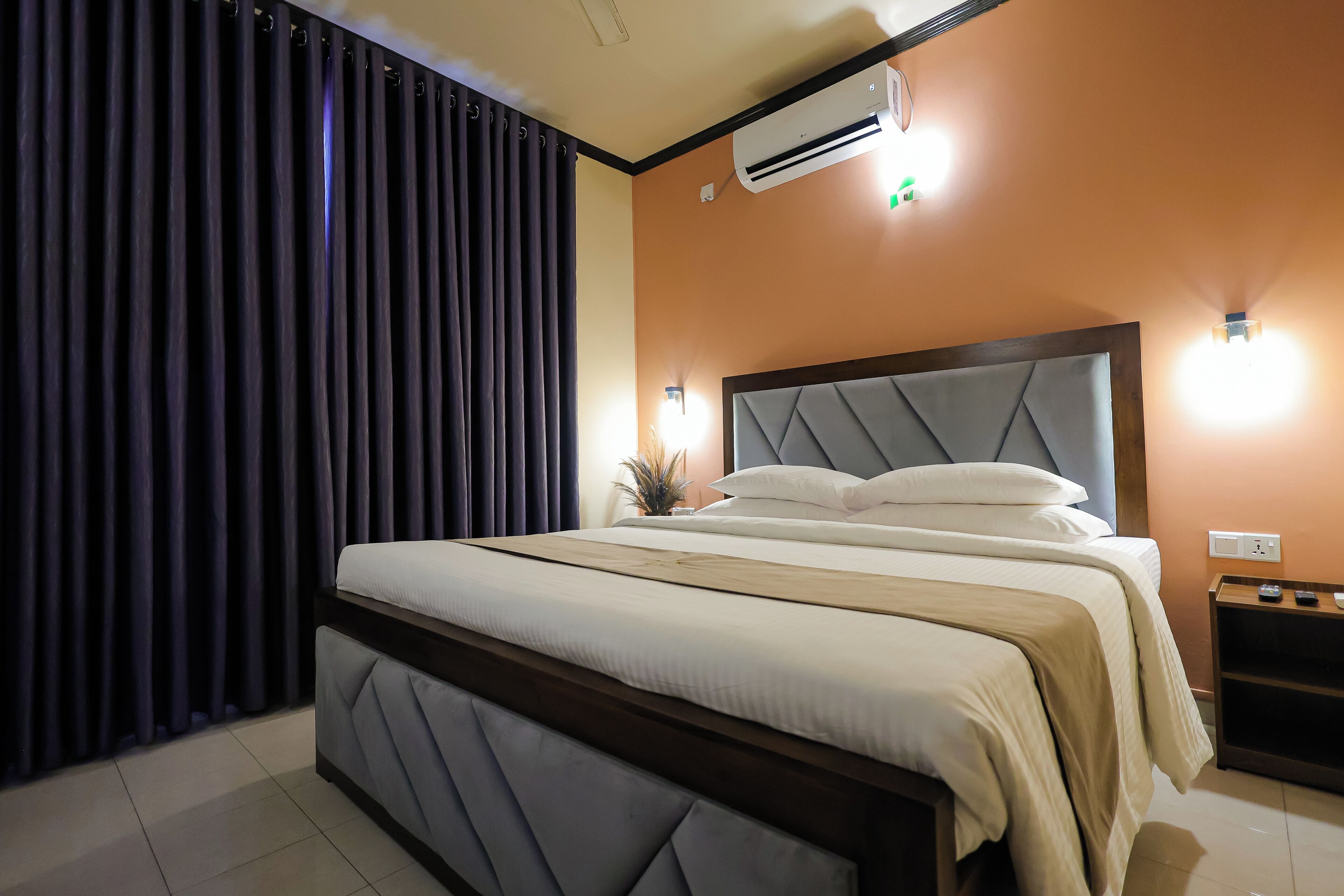 A neatly made bed with a wooden headboard, a bedside table with a lamp, and an air conditioning unit on the wall.