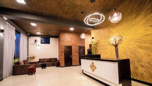 Un área de recepción moderna con pared de ladrillo, mostrador de recepción y zona de estar con sofás y una mesa de centro.