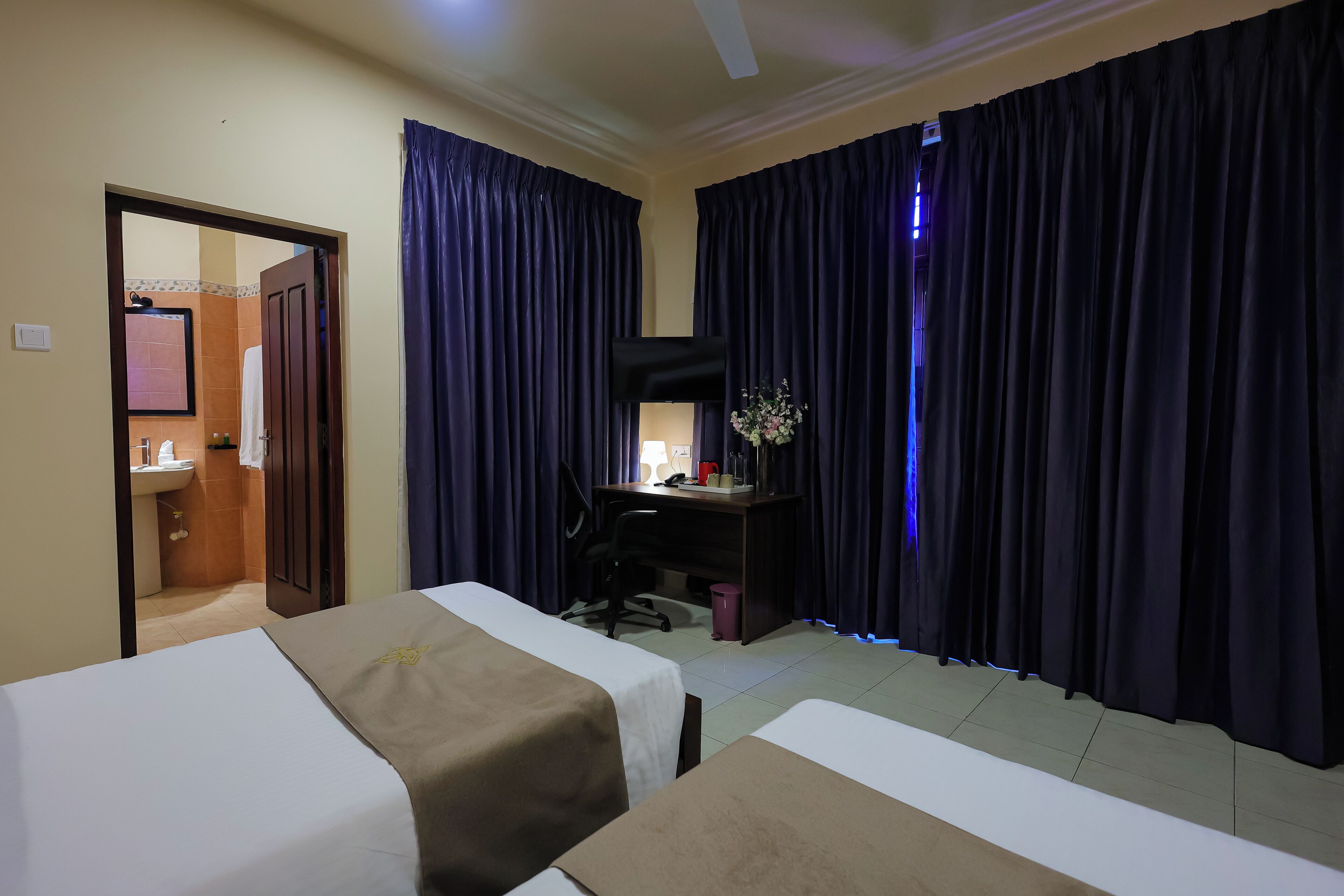 A hotel room with two beds, a desk with a computer, a mirror, and a window with curtains.