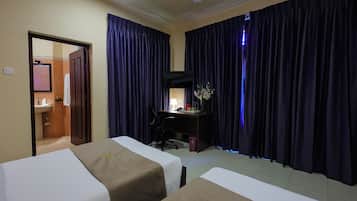Quarto de hotel com duas camas, uma escrivaninha com computador, um espelho e uma janela com cortinas.