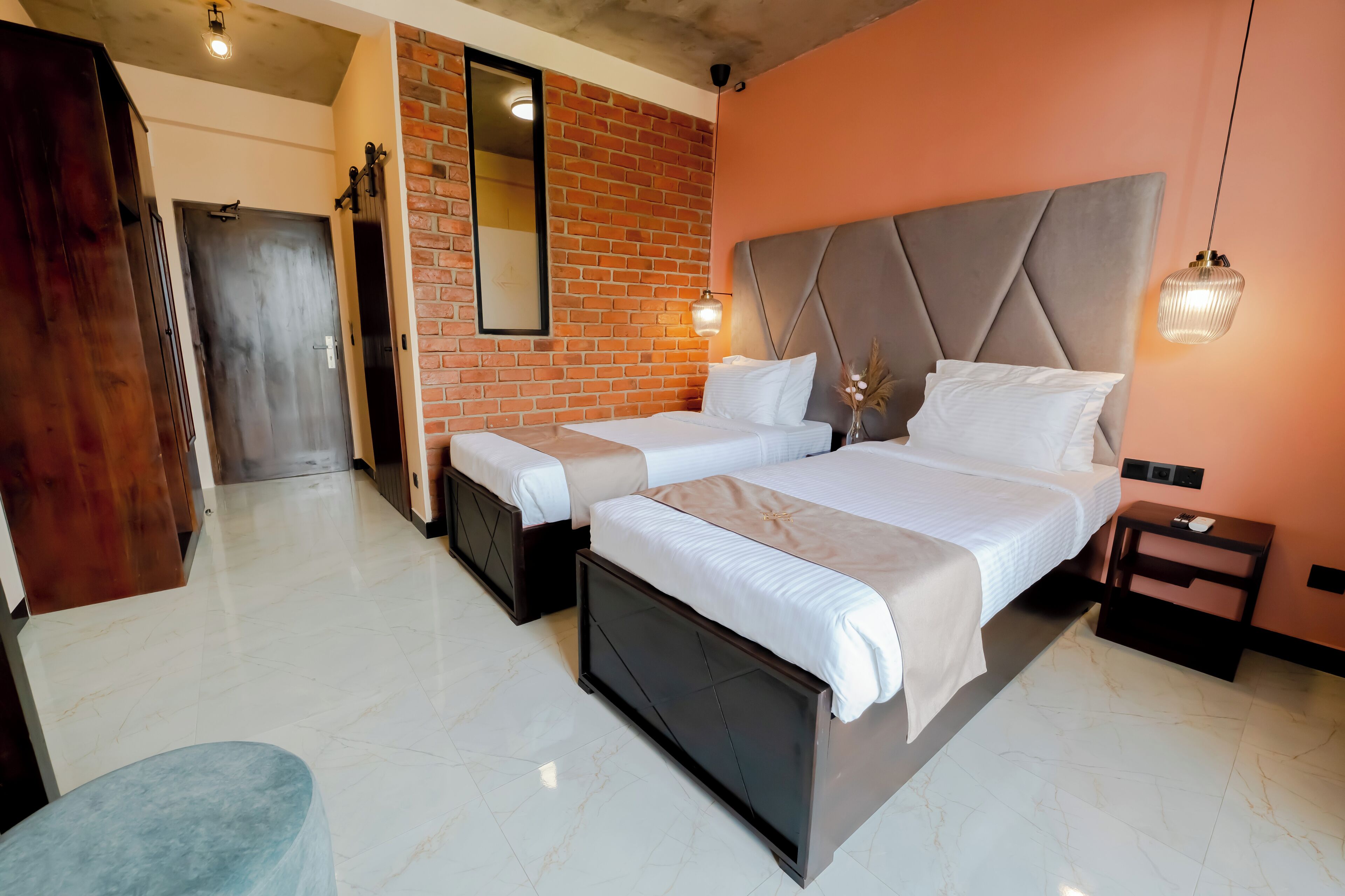 A hotel room with two beds, a brick wall, a large mirror, and a modern light fixture.
