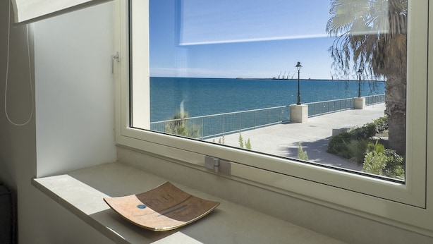 Udsigt til havet fra et vindue med en balkon, og en avis på vindueskarmen.