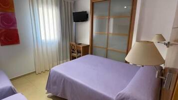 Habitación de hotel con dos camas, televisión, escritorio, silla, ventana con cortinas y puerta corredera.