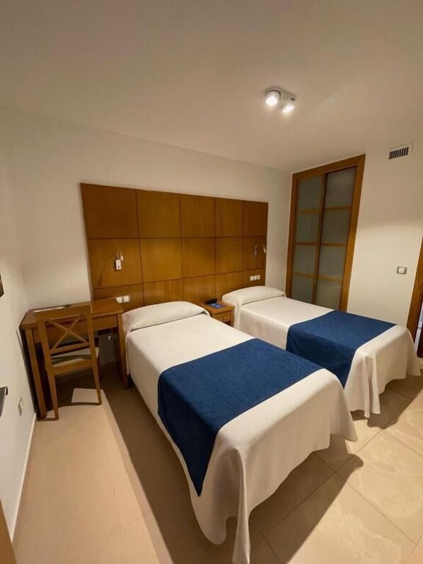 Habitación de hotel con dos camas, cabecera de madera, escritorio y una silla.