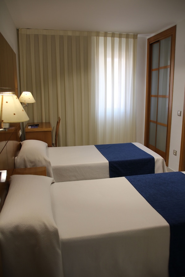 A hotel room with two beds, a desk with a lamp, a chair, and a sliding door. - HOTEL TIO PEPE (Peníscola)
