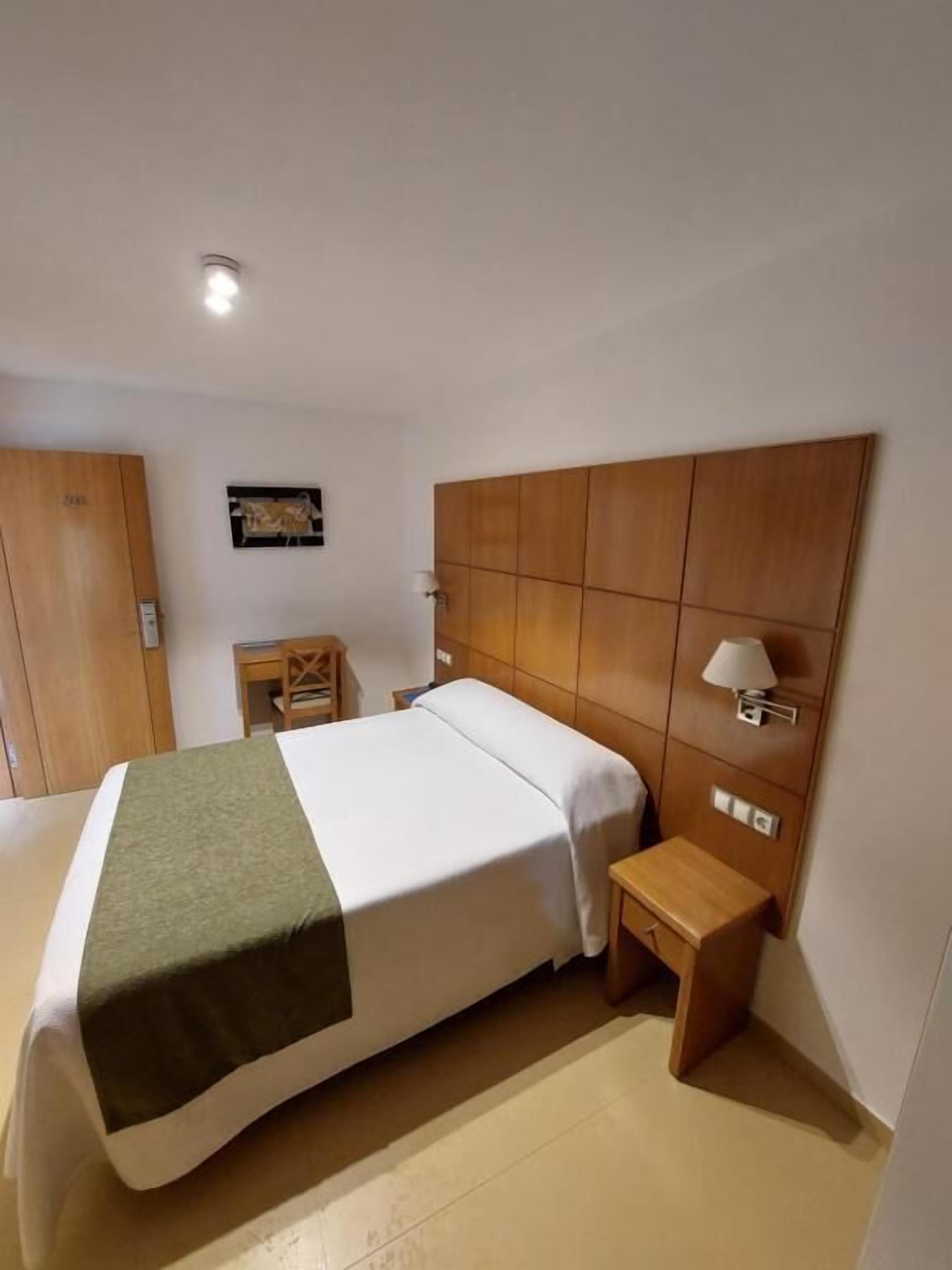 Camera d'albergo con un letto grande, una testiera in legno, un comodino con una lampada e un armadio.