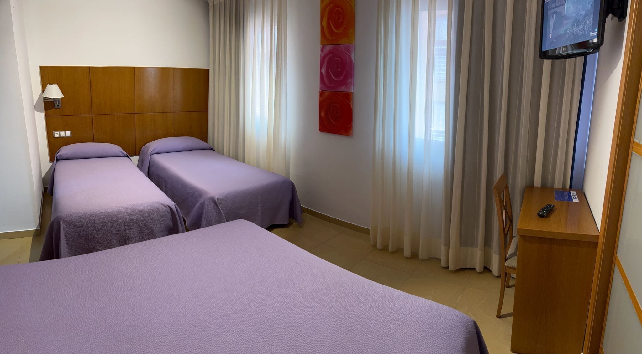 Habitación de hotel con dos camas individuales, cabecero de madera, televisor y escritorio con control remoto.