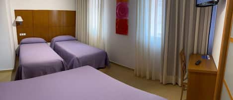 Habitación de hotel con dos camas individuales, cabecero de madera, televisor y escritorio con control remoto.
