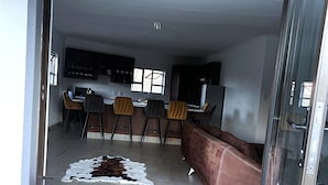 A modern kitchen with a dining area, featuring a glass door entrance, a cowhide rug, and a brown sofa. - Bikos Villa (Magaliesberg)