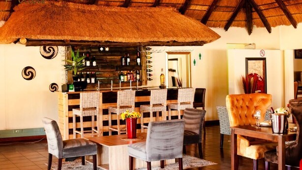 A restaurant with a thatched roof, wooden furniture, and a bar area with bottles. - Bikos Villa (Magaliesberg)